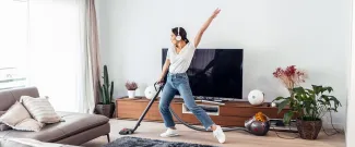 A young woman vacuuming her apartment with headphones on and dancing.